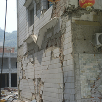 北川縣城的受損建物。除了建物表面的磁磚剝落外，也可見到許多X形龜裂。樓房越高，自身的負重越重，X形龜裂也越明顯，這是造成許多建物倒塌的主要原因。