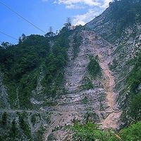 照片中的邊坡因為地震造成崩塌而露出地層的褶皺構造。稜線而下的崩塌地，不僅掩蓋下面的道路，上方的鐵塔也失去支撐顯得岌岌可危。