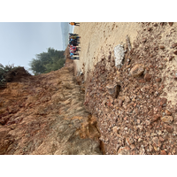 照片左側是風化的紅土層，厚達數公尺。海崖呈現海岸後退，並在坡腳產生海蝕凹壁的現象。照片中的人群，可以當成海崖高度的比例尺。
